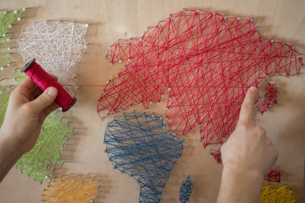 Hands creating a colorful string art map on a wooden board using vibrant threads.