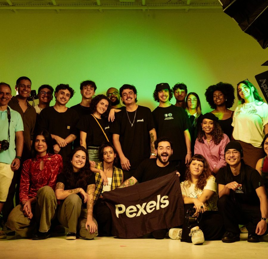 pexels-photo-33919349-33919349 A large group of diverse people posing in a professional studio setting, holding a Pexels flag.